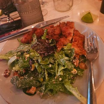 Le Chick - My Ceasar salad without Caesar dressing... - A round plate holds fried chicken pieces with a golden-brown crust and a mixed green salad featuring leafy greens, nuts, and cheese. The plate is on a table with a fork and knife, and there are glasses, a lime wedge, and a glass container in the background, indicating a dining setting. - Cocktail Bars Near Me - Miami, Florida