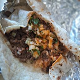 Open asada burrito. - A beef burrito filled with chopped vegetables, sauce, and meat, wrapped in a flour tortilla, partially opened and placed on aluminum foil.