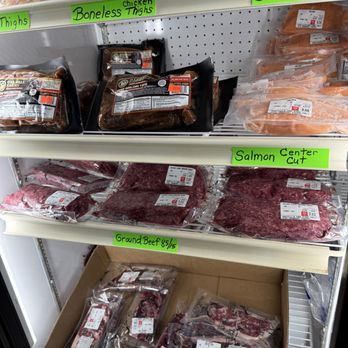 Mazzilli Farm Stand - Meat products such as chicken thighs, salmon, and ground beef are arranged on store shelves with bright green labels indicating their types and prices. - Fruits & Veggies Near Me - Wareham, Massachusetts