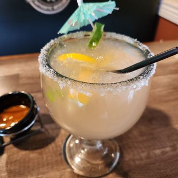 Taco Giro - Cadillac Margarita - A cocktail with a salted rim, lime wedge, and small paper umbrella in a large glass, served on a wooden table. - Mexican Near Me - Vail, Arizona
