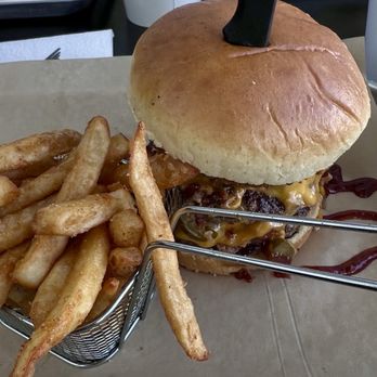 Gila Hogs BBQ - A yummy jalapeño burger - A cheeseburger with a bun, melted cheese, and beef patty is presented with a side of French fries in a small metal basket. - Barbeque Near Me - Globe, Arizona