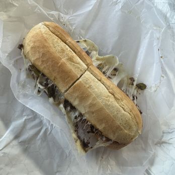 Algonquin Sub Shop - Cheezy Italian Beef with Sweet Peppers - A sandwich with melted cheese and dark ingredients on a bun, partially cut, placed on white paper, served at Algonquin Sub Shop. - Sandwiches Near Me - Algonquin, Illinois