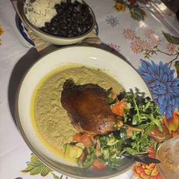Bombera - A meal featuring a roasted chicken leg served with green sauce and a side salad of tomatoes, cucumbers, and greens. A bowl of rice and black beans is also visible. - Mexican Near Me - Oakland, California