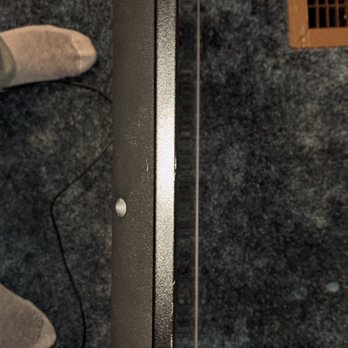 Marathon Moving - Scratches on the top of the TV - The image shows the top edge of a flat-screen TV with scratches on its surface, set against a dark carpeted floor. - Movers Near Me - Canton, Massachusetts