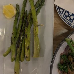 Asparagus - A plate of grilled asparagus spears with char marks, accompanied by a lemon wedge, on a white rectangular plate.