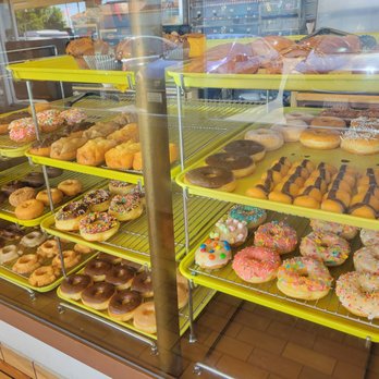405 Donut - a variety of doughnuts in a display case - A bakery display case showcases a variety of donuts with colorful toppings, sprinkles, and chocolate drizzle, along with other baked goods. - Donuts Near Me - Orange, California
