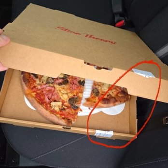 Slice Theory - A pizza box is partially opened, revealing a slice of pizza with toppings including ham, mushrooms, and cheese. The box is placed on a black surface, possibly a car seat, and has a barcode sticker on the lid. The pizza appears to have a crispy crust and is served in a typical takeout container. - Pizza Near Me - Ashburn, Virginia