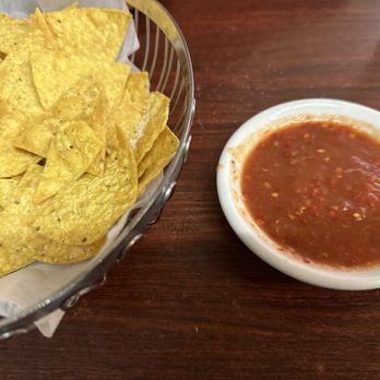 El Comal - Chips with hot, hot salsa - A basket filled with tortilla chips and a small bowl of red salsa are placed on a wooden table, typical of Mexican cuisine. - Mexican Near Me - Santa Fe, New Mexico