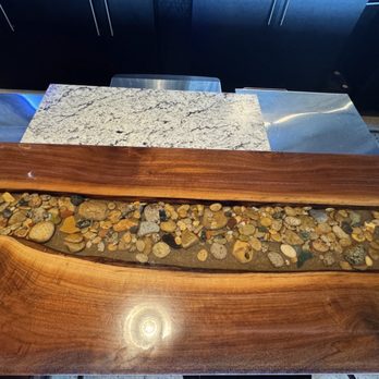 Stone Hound Brewing - Beautiful live edge bar top. - The image shows a bar top featuring a live edge wood slab with a river of small pebbles embedded in the center, situated in a bar setting. - Breweries Near Me - Williamsburg, Michigan