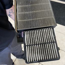 My super-dirty air filters they recommended for replacement. - A person is holding two used, dirty car air filters, showing signs of dirt and debris buildup, in a retail or service environment.