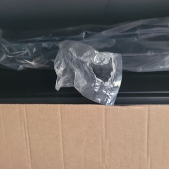 McGee Toyota of Epping - The screws package clearly ripped open and empty. In my "new" part. - The image shows a cardboard box with vertical ridges, containing a clear plastic bag. Inside the bag, there is a torn piece of plastic, which appears crumpled and partially transparent. The background suggests an indoor setting, and the focus is on the contents of the box, highlighting the torn plastic piece. - Car Dealers Near Me - Epping, New Hampshire