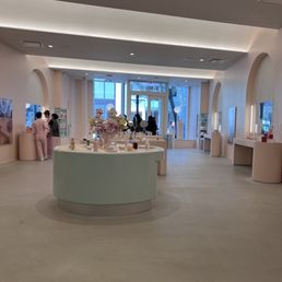 A spacious, well-lit beauty store features display tables with skincare and makeup products, and customers browsing near the windows.