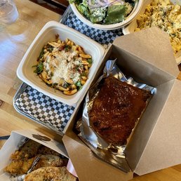 Assorted food items including a salad with onions, pasta with cheese, glazed ribs, fried chicken, and macaroni and cheese on a wooden table.