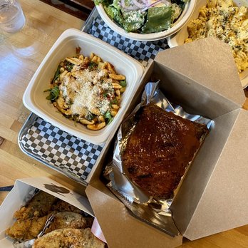 The Rook - Assorted food items including a salad with onions, pasta with cheese, glazed ribs, fried chicken, and macaroni and cheese on a wooden table. - New American Near Me - Ithaca, New York