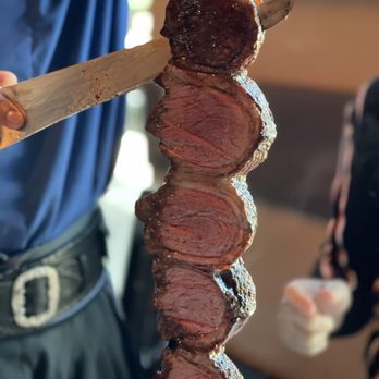 Texas de Brazil - Addison - a man holding a knife and cutting a steak - Brazilian Near Me - Addison, Texas