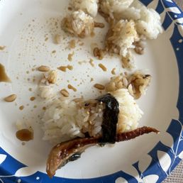 Eel sushi - A paper plate with remnants of sushi, including rice, eel, sesame seeds, and soy sauce, is shown. The plate has a blue and white floral border.