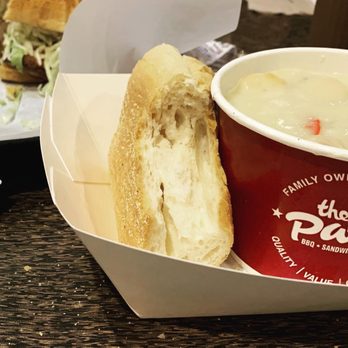 The Patio - A bread roll and a cup of soup are placed in a white container on a dark wooden table, with a burger in the background. - Barbeque Near Me - Lombard, Illinois