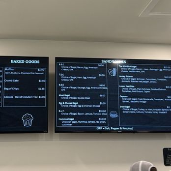 Time 4 Bagels - Bagels and sandwich options. 2.00 for regular bagels but extra .50 for some of the premium ones like Asiago and jalapeño cheddar - Three digital menu screens display food and drink options at a bagel shop. The first screen lists bagel prices and spreads, including cream cheese, specialty CC, and peanut butter. The second screen features sandwich options like egg, smoked salmon, and cheese bagels, with prices. The third screen shows coffee and tea choices, bottled water, and other drinks, with prices. The menu layout is clear and organized for customer ordering. - Bagels Near Me - Gainesville, Virginia