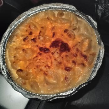 High Point Grill - The original baked mac - A baked macaroni and cheese dish with a golden-brown crust in a round foil container, placed on a dark surface. - Sandwiches Near Me - Albuquerque, New Mexico