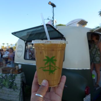 Ahimsa Caravan Cafe - a hand holding a cup of iced coffee - Food Trucks Near Me