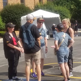 Chicago Plumbers Union Hall - Five individuals are gathered outdoors on a sunny day, engaged in conversation near a white canopy tent, with a brick building and greenery in the background. - Venues & Event Spaces Near Me - Chicago, Illinois