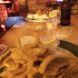 Perch Plate - Plate of fried fish fillets with French fries, lemon slices, and dipping sauces on a wooden table in a restaurant setting.
