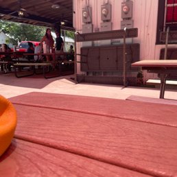 Outdoor space - An outdoor dining area with picnic tables, some people standing and talking, and electrical meters on a pink building wall.