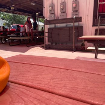The Loose Caboose - Outdoor space - An outdoor dining area with picnic tables, some people standing and talking, and electrical meters on a pink building wall. - Barbeque Near Me - Spring, Texas