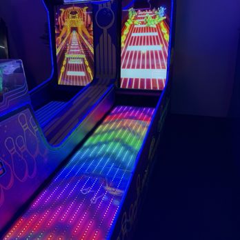 Zoocade - The image shows an arcade game called 'Lane Master Xtreme' with illuminated LED lanes and colorful neon lighting. The game has a vertical screen displaying a game interface with bright graphics, and the LED lanes are decorated with rainbow-colored lights. The surrounding environment is dark, emphasizing the vivid lighting effects of the arcade machine. - Arcades Near Me - Austin, Texas