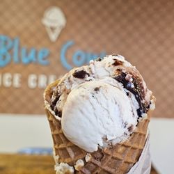 A Waffle Cone with a scoop of Peanut Butter Fudge Ice Cream in front of the new Waffle Cone look wall and shop logo.