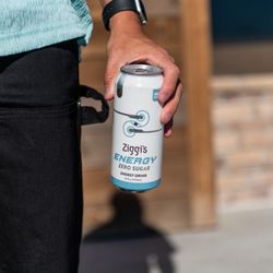 Ziggi's Coffee - Person holding a Ziggi's Energy Zero Sugar can outside near a storefront.
