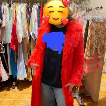 Una Mae's - A person in a red faux fur coat stands in a clothing store with racks of colorful garments behind them. - Women's Clothing Near Me - Chicago, Illinois