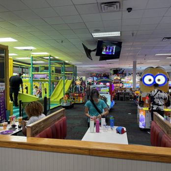 Chuck E. Cheese - Indoor arcade at Chuck E. Cheese featuring arcade games, a play structure, and dining tables with people enjoying food and activities. - Pizza Near Me - Skokie, Illinois