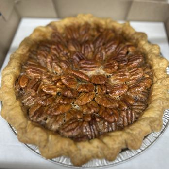 Tiny Pies - A pecan pie featuring a golden, flaky crust with a crimped edge. The filling is topped with a layer of glazed pecans arranged in a circular pattern. The pie is in a disposable aluminum pie pan, inside a cardboard box, ready for serving or delivery. - Desserts Near Me - Austin, Texas