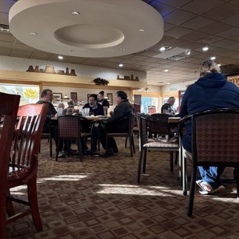Copper Canyon Cafe - A woman wearing a blue hoodie and jeans sits alone at a table in a restaurant, with other groups of people dining in the background. - Mexican Near Me - Albuquerque, New Mexico