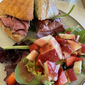 Panicafé - Beautiful beef pastrami sandwich plate - A beef pastrami sandwich on a baguette with greens, served with a mixed fruit salad on a plate at a cafe. - Bakeries Near Me - Spring, Texas