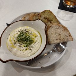Whipped Feta - A dish of whipped feta topped with chopped green onions and herbs, served with slices of bread, on a white plate and table.