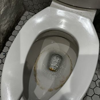 Parish - Moldy toilet hasn't been cleaned in months but they are charging $16 a cocktail - A white toilet with a stained bowl and dirt around the rim, situated in a bathroom with hexagonal tile flooring and a stone wall. - Music Venues Near Me - Austin, Texas
