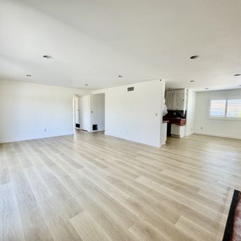 Divinity Flooring Services - A large, empty living room with light wood flooring, white walls, and multiple windows allowing natural light. - Flooring Near Me