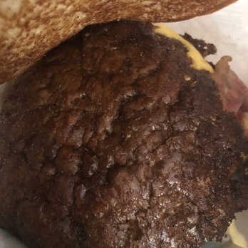 Culver's - The image features a cooked beef patty with a dark, textured surface, indicating it has been grilled or fried. The patty is positioned beneath a toasted bun, which is partially visible at the top of the image. The background includes a piece of paper or wrapper, suggesting the burger is served in a casual setting. - Burgers Near Me - Ottawa, Illinois