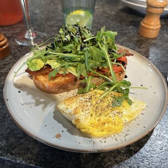 Bonfire Grill - Avocado toast - A plate features avocado toast topped with greens and drizzled with balsamic glaze, alongside a fried egg, on a dark restaurant table. - New American Near Me - Tomball, Texas