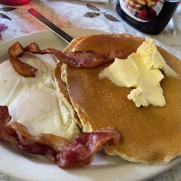 Two large and fluffy pancakes topped with butter. 2 eggs. 2 strips of bacon. Two large and fluffy pancakes topped with butter. 2 eggs. 2 strips of bacon.