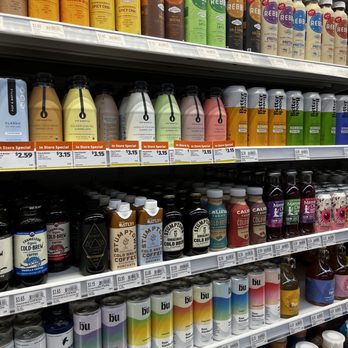 Natural Grocers - a variety of drinks - Store shelves at Natural Grocers in Albuquerque, NM, stocked with a variety of bottled coffee, tea, and beverage drinks. The top shelf features REBBL brand drinks in different flavors, while the middle shelves include Califa Farms cold brew coffee and BU canned drinks. Price tags are visible, indicating the cost of each product. The arrangement showcases a selection of plant-based and specialty beverages available for purchase. - Grocery Near Me - Albuquerque, New Mexico
