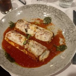 Cannelloni - A plate of cannelloni pasta topped with melted cheese, served on a decorative ceramic plate with tomato sauce and green pesto dollops.
