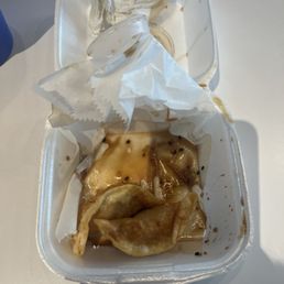 Poke Bowl - A foam takeout container holds leftover food, including a fried dumpling and some sauce, with crumpled napkins inside.