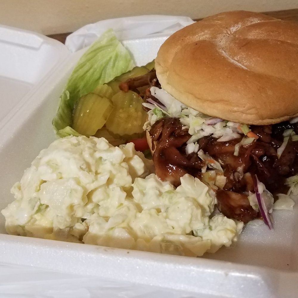The Grill - Pulled pork sandwich, potato salad, and pickles. The sandwich comes with coleslaw topped on the bbq pulled pork. - American Near Me - Lone Pine, California The Grill - Pulled pork sandwich, potato salad, and pickles. The sandwich comes with coleslaw topped on the bbq pulled pork. - American Near Me - Lone Pine, California