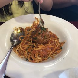 Meatballs - Spaghetti with meatball and tomato sauce served on a white plate, with a spoon and fork, in a restaurant setting.