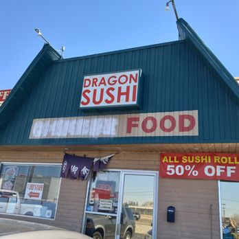 Dragon Sushi - The image shows the front of Dragon Sushi, a sushi restaurant with a large sign displaying its name. A red banner advertises a 50% discount on all sushi rolls. The building has a brick facade, windows, and an entrance door with an 'OPEN' sign. The sky is clear and blue, and there are parked cars visible in the reflection of the windows. - Sushi Bars Near Me - Albuquerque, New Mexico