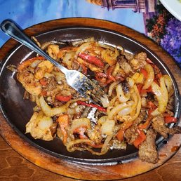 This is an uneaten plate of chicken and steak fajitas. It's full of onions and peppers. This is an uneaten plate of chicken and steak fajitas. It's full of onions and peppers.