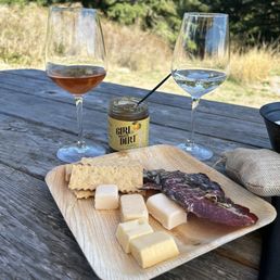 a plate of cheese, crackers, and wine on a picnic table